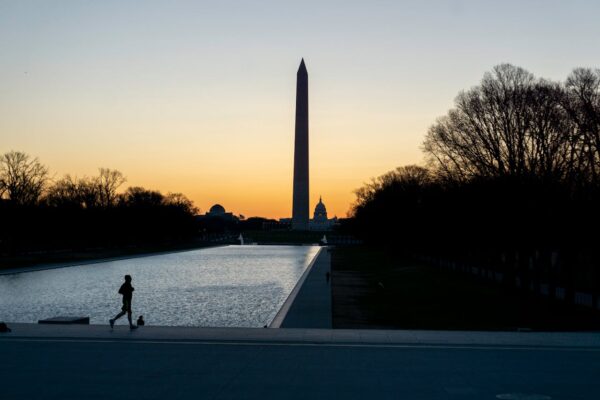 Jogger at sunset with the silhouette of the Washington Monument and the Capitol Building in the background.